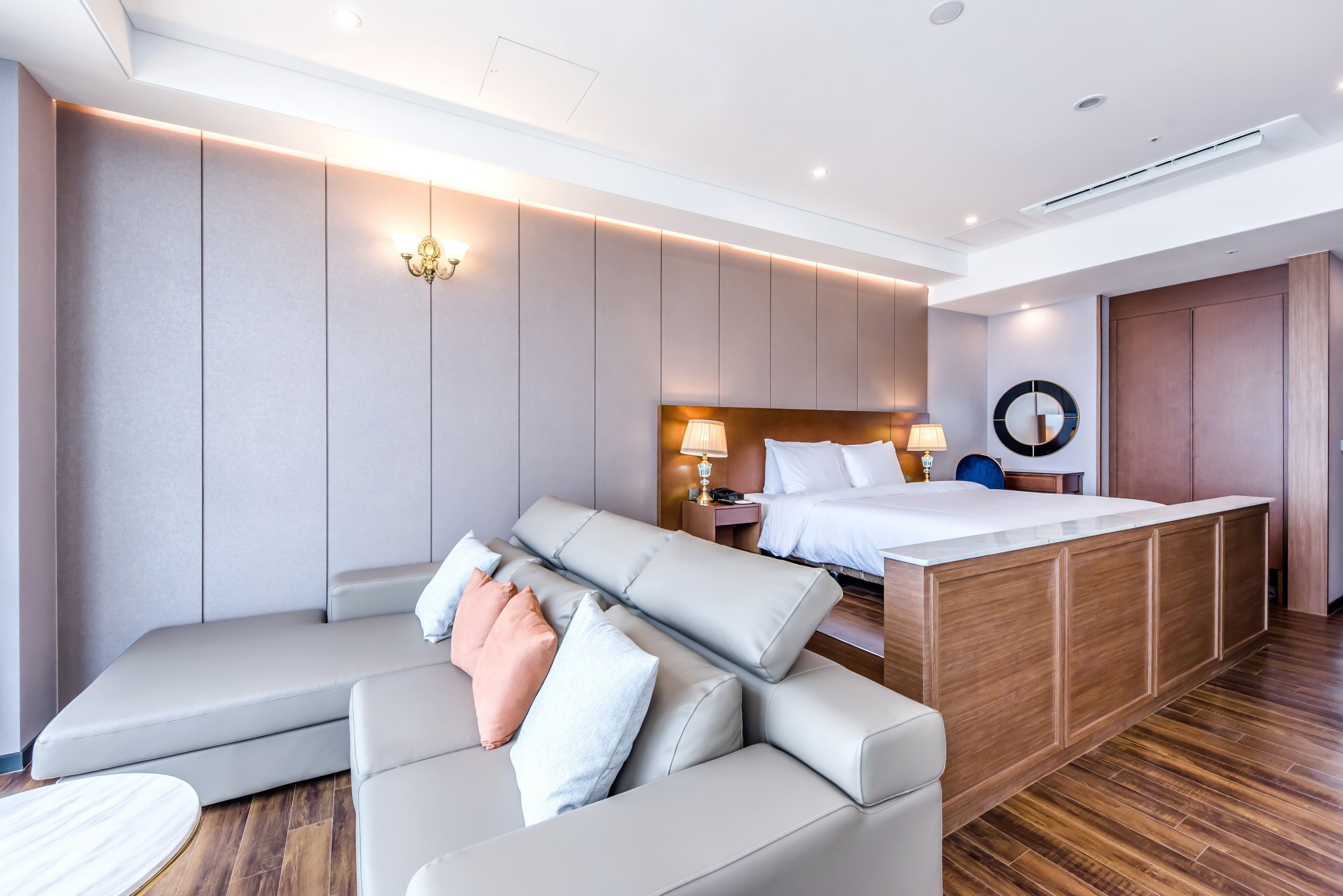 Een moderne hotelkamer met een grote bank, een bed met een houten hoofdeinde, een klein tafeltje en een inbouwkantoor.