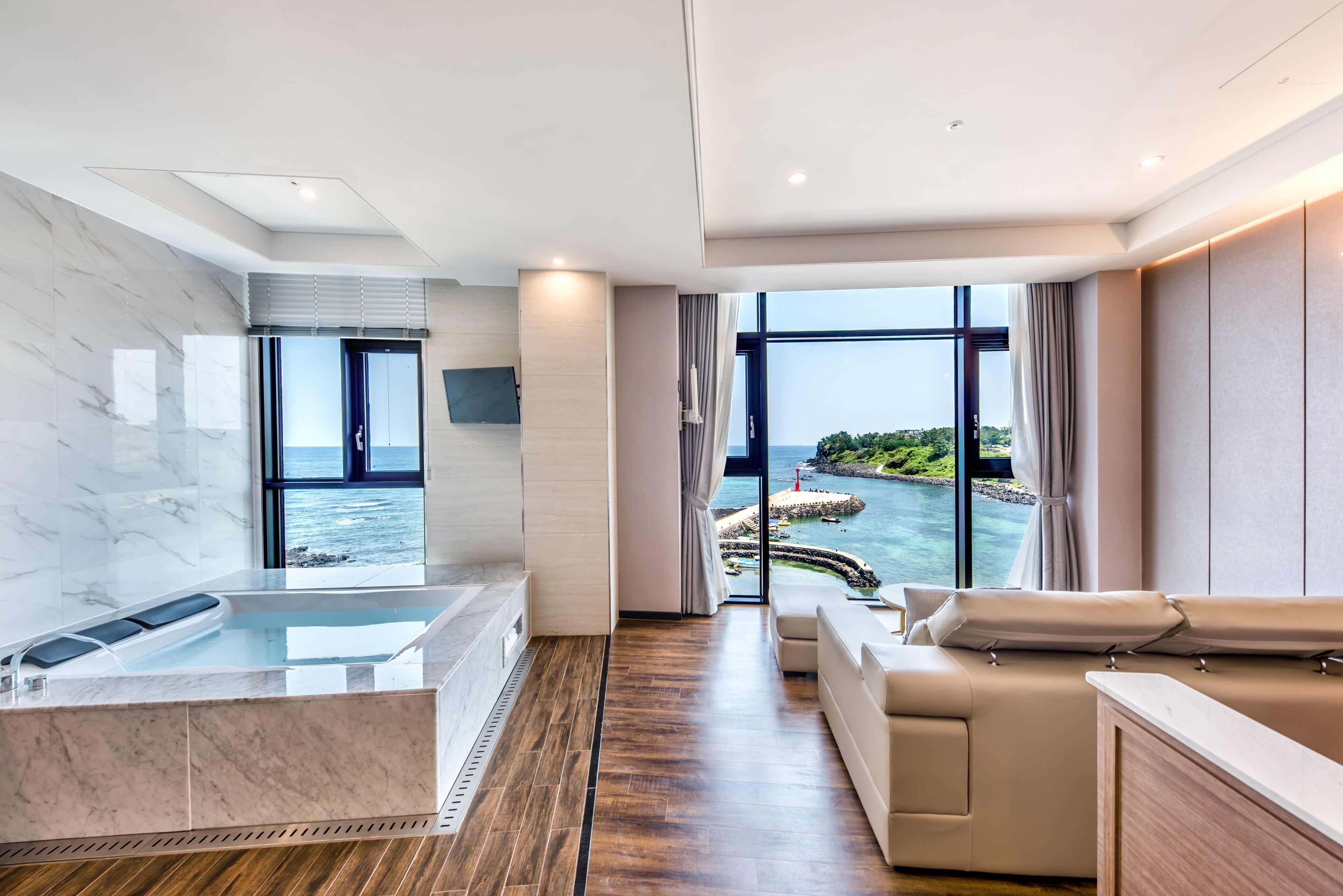 Un hotel moderno con una ventana grande que ofrece vista al mar, una bañera de mármol y un rincón de descanso acogedor.