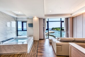 Un hotel moderno con una ventana grande que ofrece vista al mar, una bañera de mármol y un rincón de descanso acogedor.