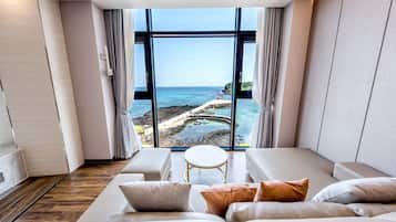 A modern room with a large window offering a view of a rocky coastline and the sea.