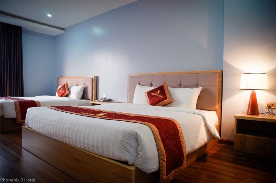 A hotel room with two beds, a wooden headboard, a red throw blanket, and a bedside lamp.