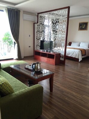 A hotel room with a sofa, a coffee table, a TV on a stand, a bed, and a decorative partition. - Phoenix 3 International Hotel (Kinh Bac)