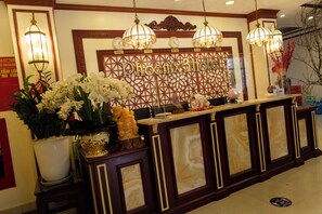 A hotel reception desk with a decorative wall featuring city names, a large white flower arrangement, and a clock. - Phoenix 3 International Hotel (Kinh Bac)