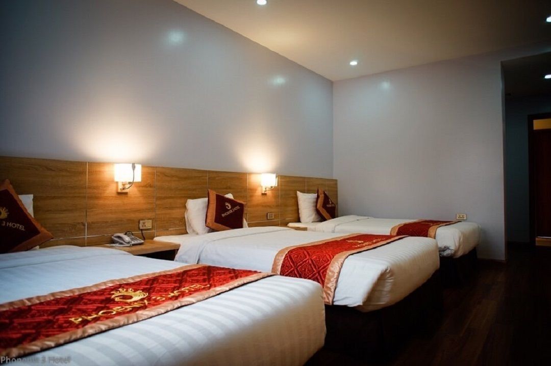 A hotel room with three beds, each with a red and white bedspread, and a wooden headboard.