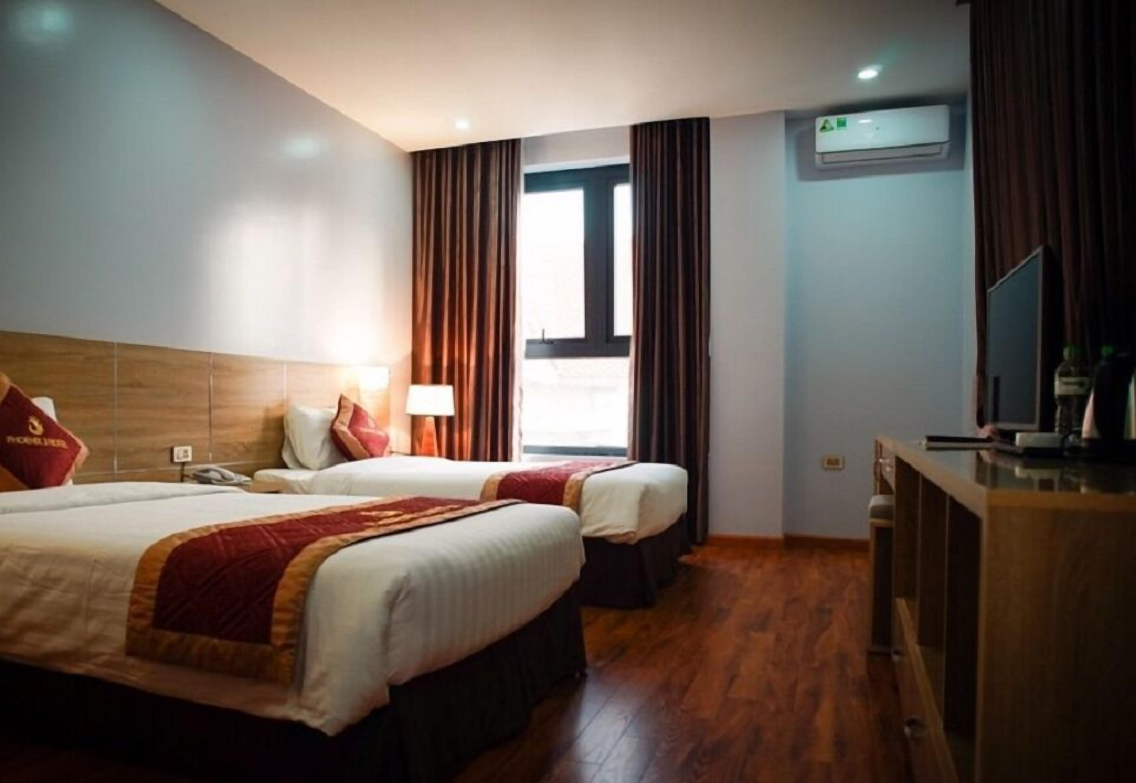 A hotel room with two beds, a desk, a TV, and an air conditioning unit.