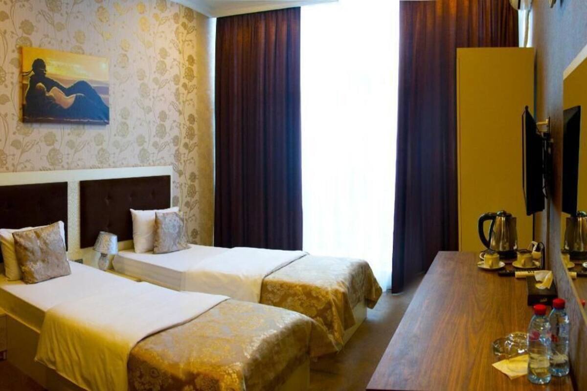 A hotel room with two beds, a wooden desk, a telephone, and a painting on the wall.