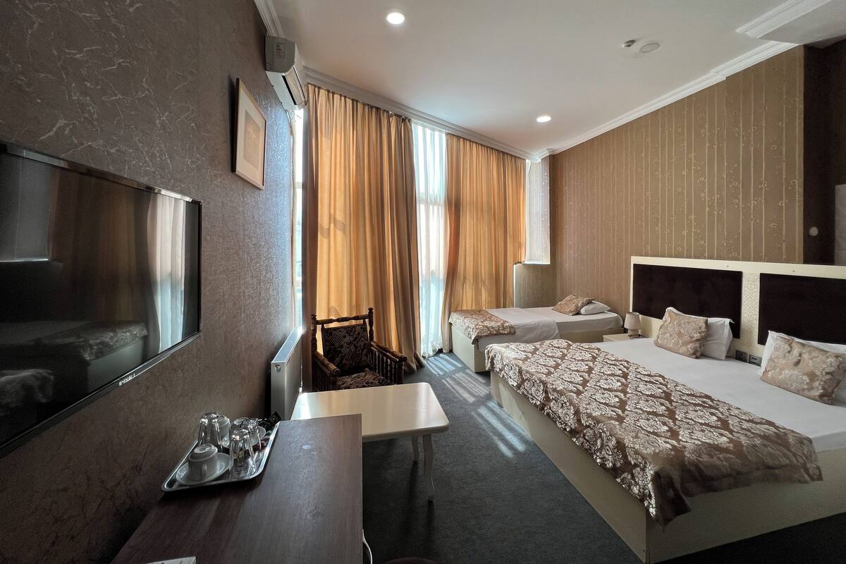 A hotel room with a bed, a desk, a chair, a TV, and a window with curtains.