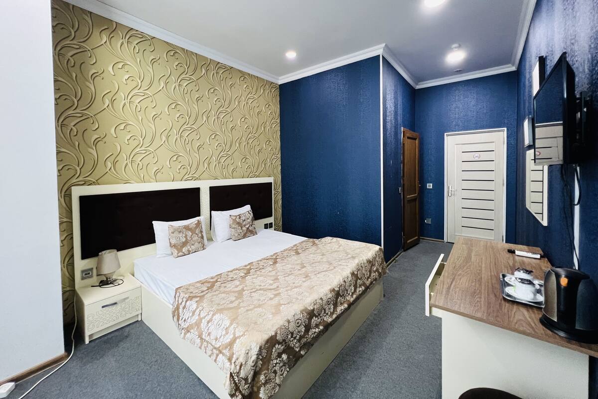 A bedroom with a large bed, a desk with a coffee maker, and a TV on the wall.
