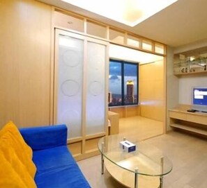 Una sala de estar moderna con un sofá azul, una mesa de centro de vidrio y vistas a un paisaje urbano a través de un ventanal grande.