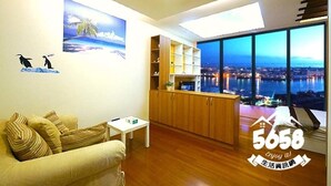 Una sala de estar moderna con un amplio ventanal que ofrece vistas a la ciudad, una zona de cocina con armarios de madera y un sofá con cojines estampados.
