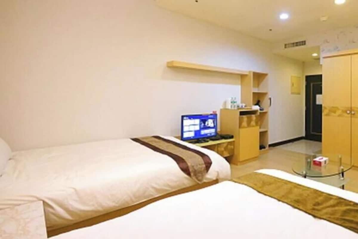 Habitación de hotel con dos camas, un escritorio con computadora, un armario y una mesita.