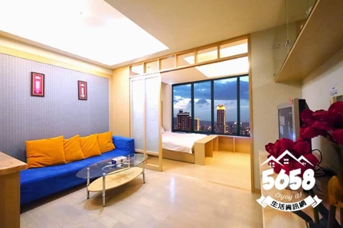 Una habitación de hotel moderna con sofá, cama, una mesita de centro de vidrio y un ventanal con vista a la ciudad.