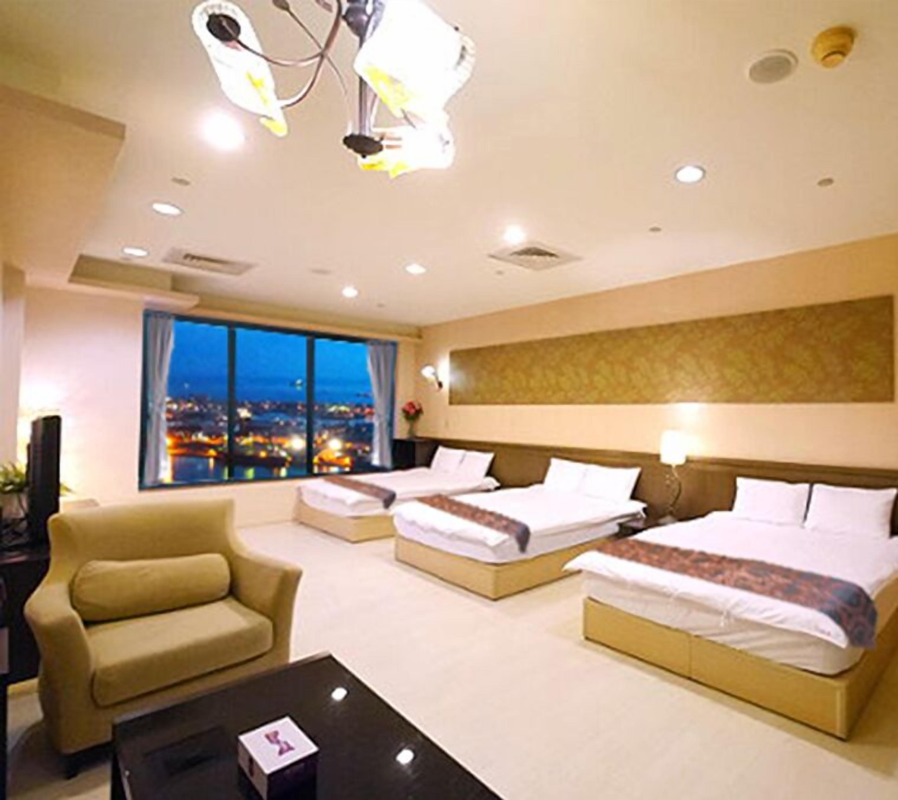 A hotel room with two beds, a sofa, a coffee table, and a large window with a city view.