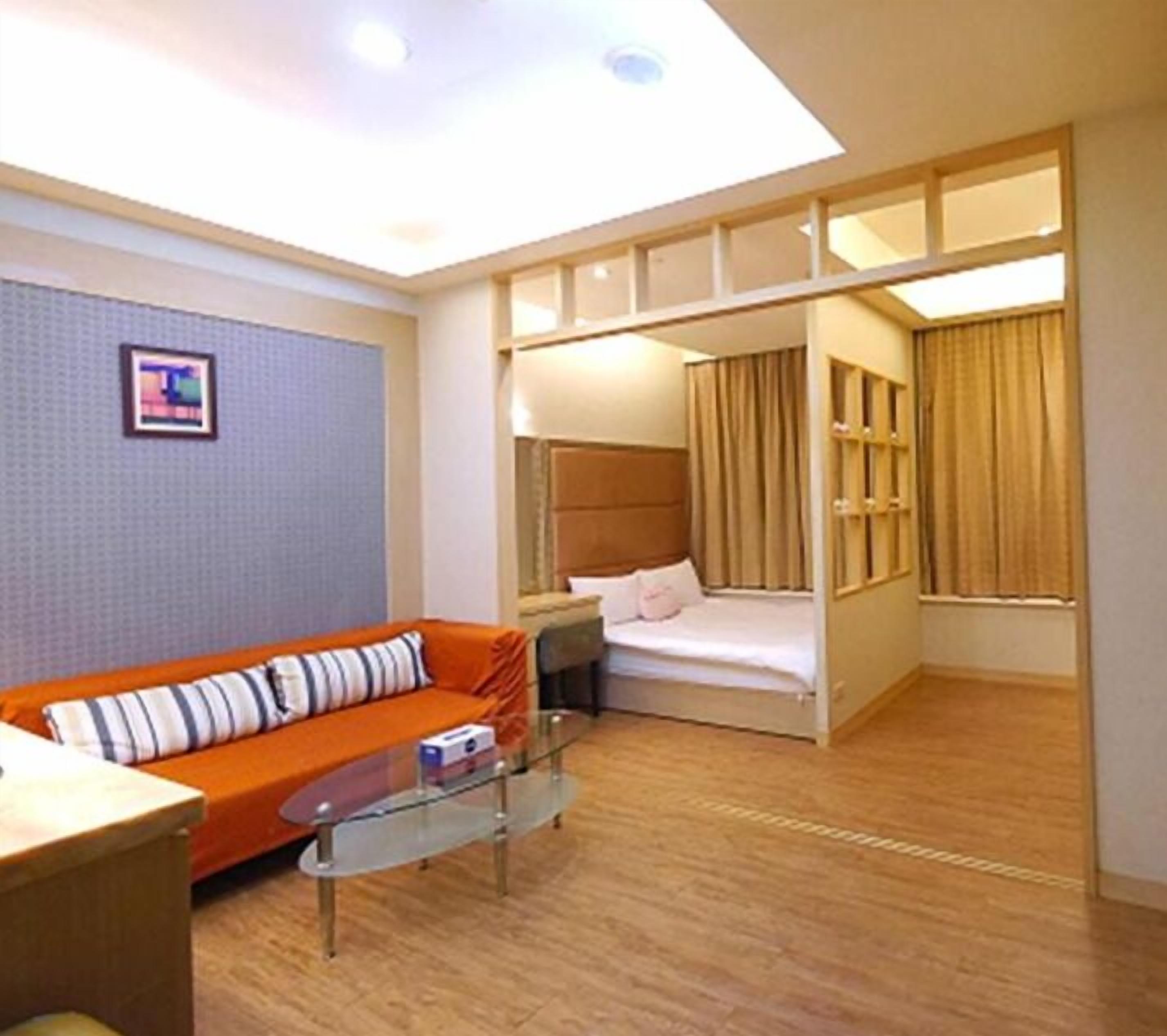 A compact hotel room with a sofa, a bed, a glass coffee table, and a wardrobe.