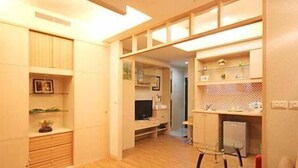 Un espacio habitable compacto con estanterías empotradas, televisor y una pequeña zona de kitchenette.