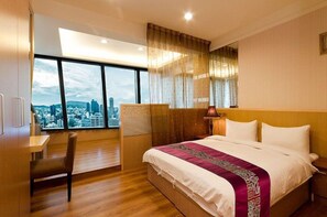 Habitación de hotel con una cama grande, un escritorio y una silla. Se ve una ventana con vista a la ciudad.