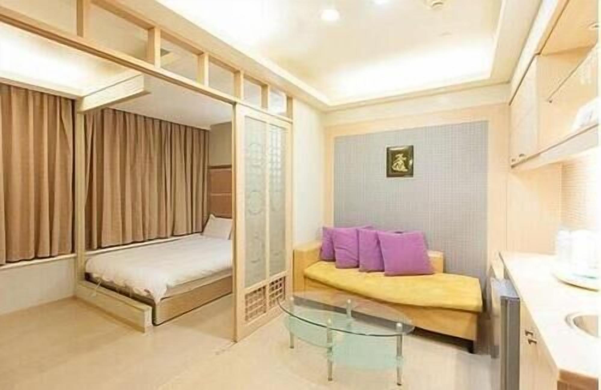 A compact hotel room with a bunk bed, a sofa with cushions, a glass coffee table, and a small TV.