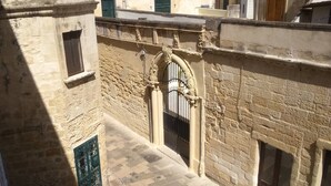 A narrow alleyway with a stone wall, a metal gate, and a small window. - Palazzo Marturano (Lecce)