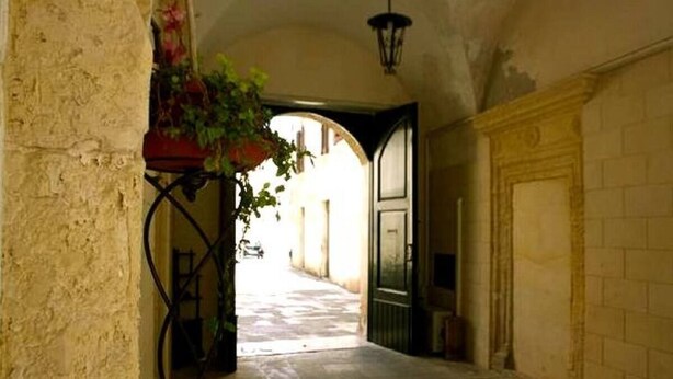 An arched hallway with a stone wall on one side and a door on the other. - Palazzo Marturano (Lecce)