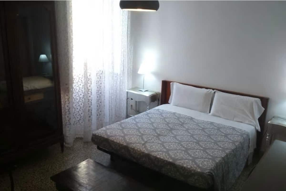 A bedroom with a bed, bedside table, lamp, and a wardrobe.