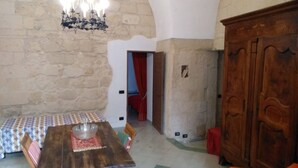 A dining area with a wooden table, chairs, a chandelier, and a stone wall. - Palazzo Marturano (Lecce)