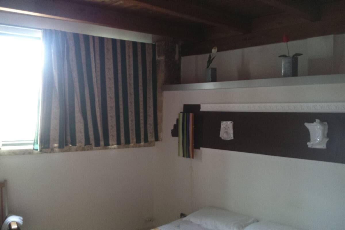 A room with a bed, a window with striped curtains, and a shelf with decorative items.
