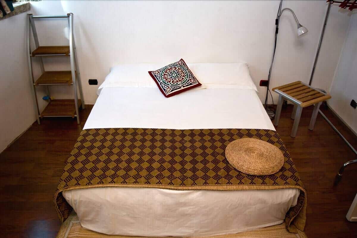 A neatly made bed with a patterned bedspread, a decorative pillow, and a small wooden stool.