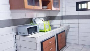 Eine Küche mit weißen Fliesen, einer Mikrowelle, einem grünen Geschirrgestell und Holzschränken.