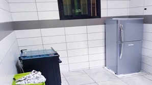 Eine kleine Küche mit weißen und grauen Fliesen, einem kleinen Fenster, einem Kühlschrank und einem Wagen mit Körben.