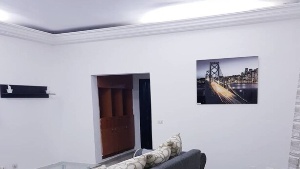 Ein modernes Wohnzimmer mit grauem Sofa, einem Glastisch und einem Stadtbild an der Wand.