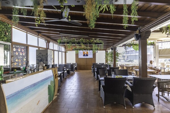 A restaurant with a long counter, hanging plants, and outdoor seating. - Hotel Gala (Noja)