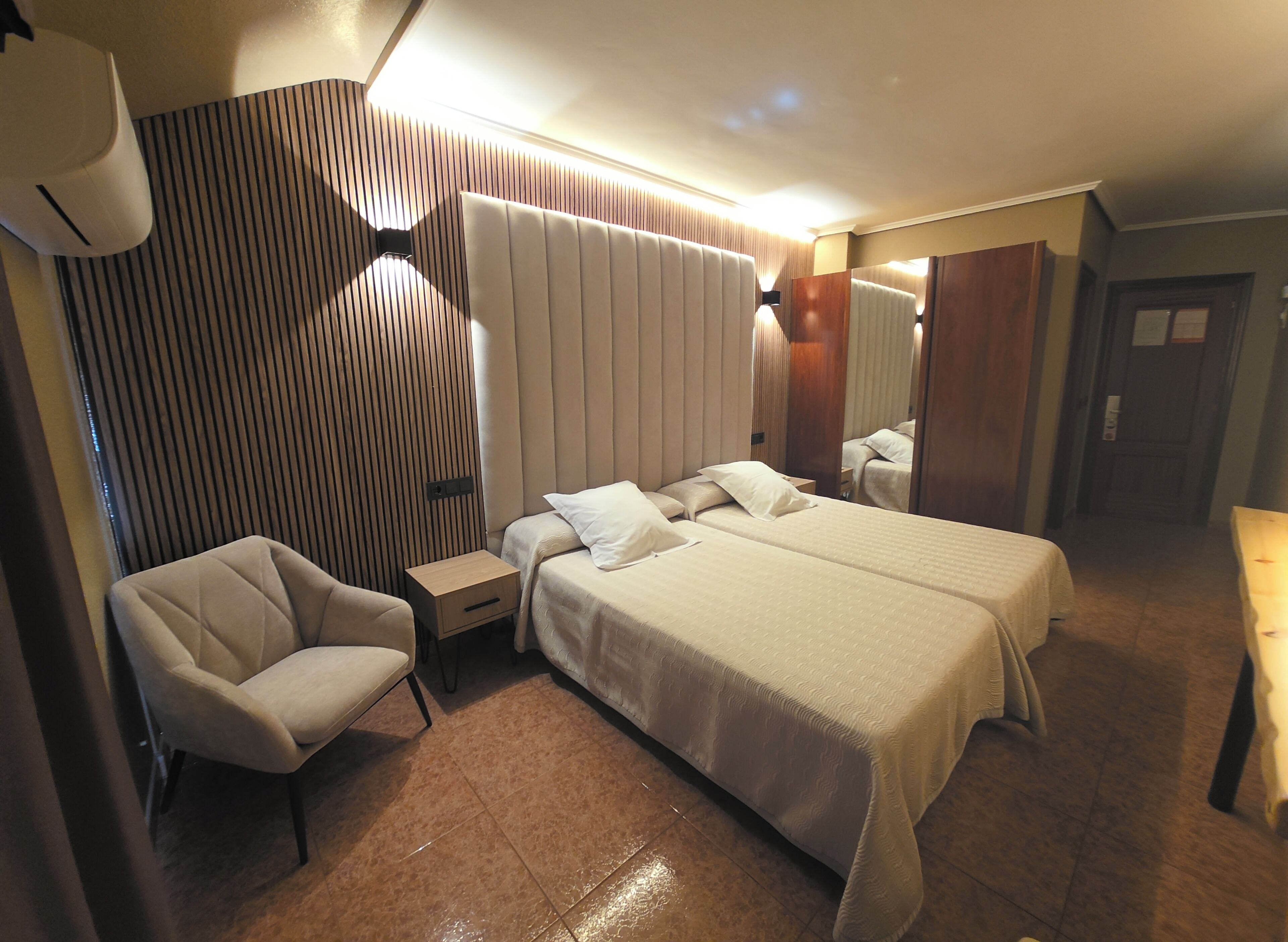 Una habitación de hotel con una cama grande, dos mesitas de noche, una silla y un espejo.