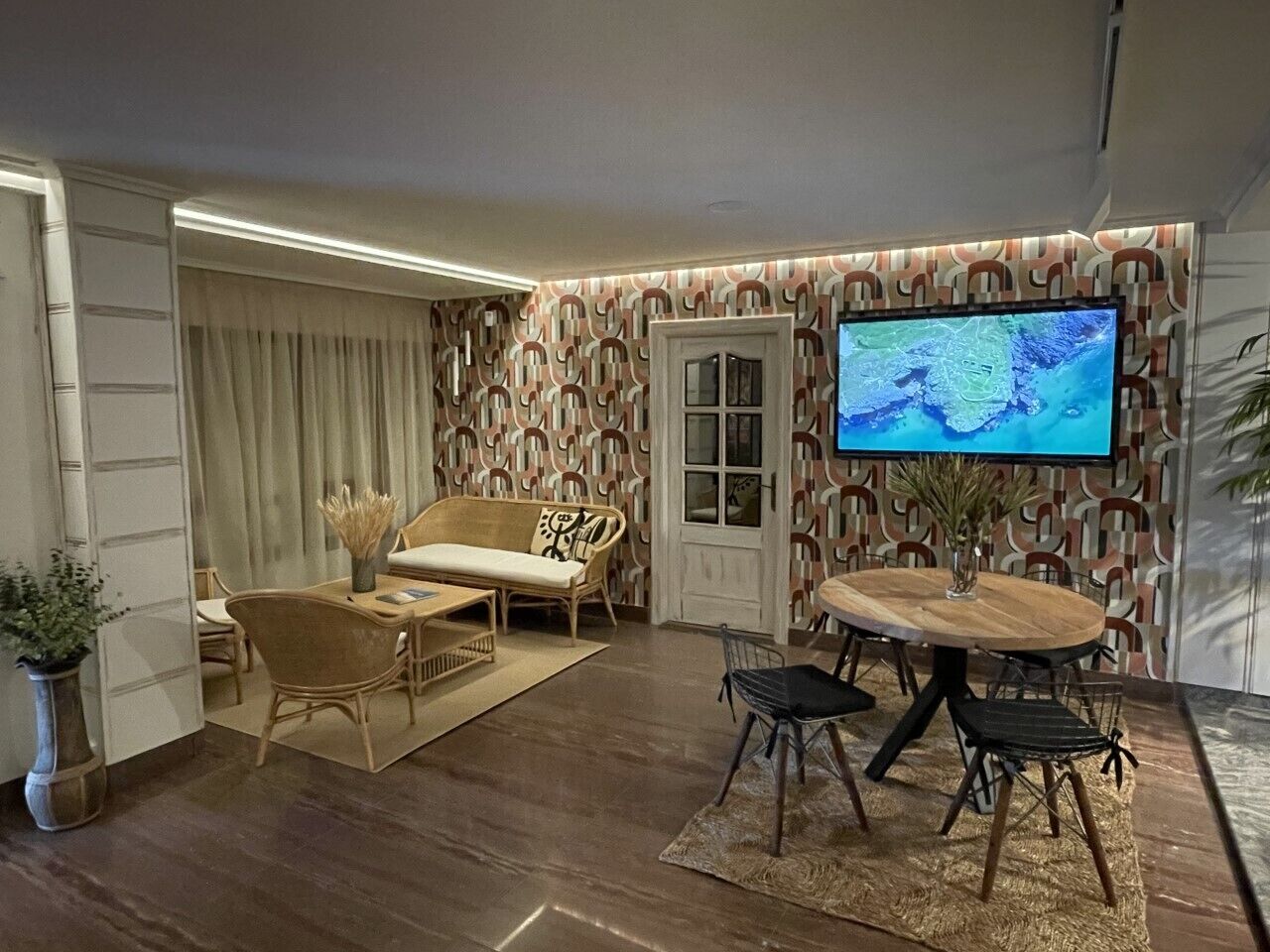 A modern living room with a wooden dining table, two sofas, and a TV mounted on the wall.