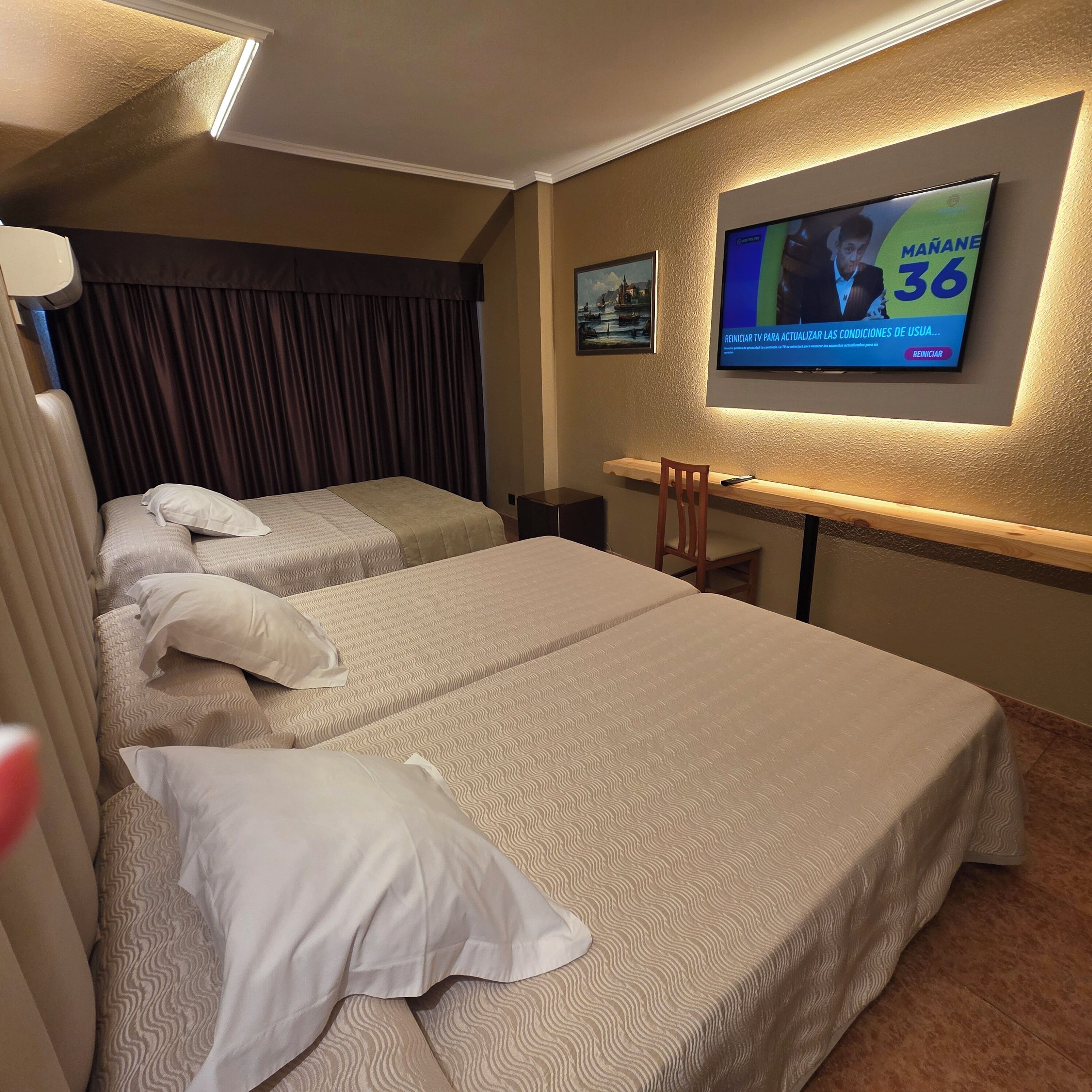 Ein Hotelzimmer mit zwei Betten, einem an der Wand befestigten Fernseher und einem Schreibtisch.