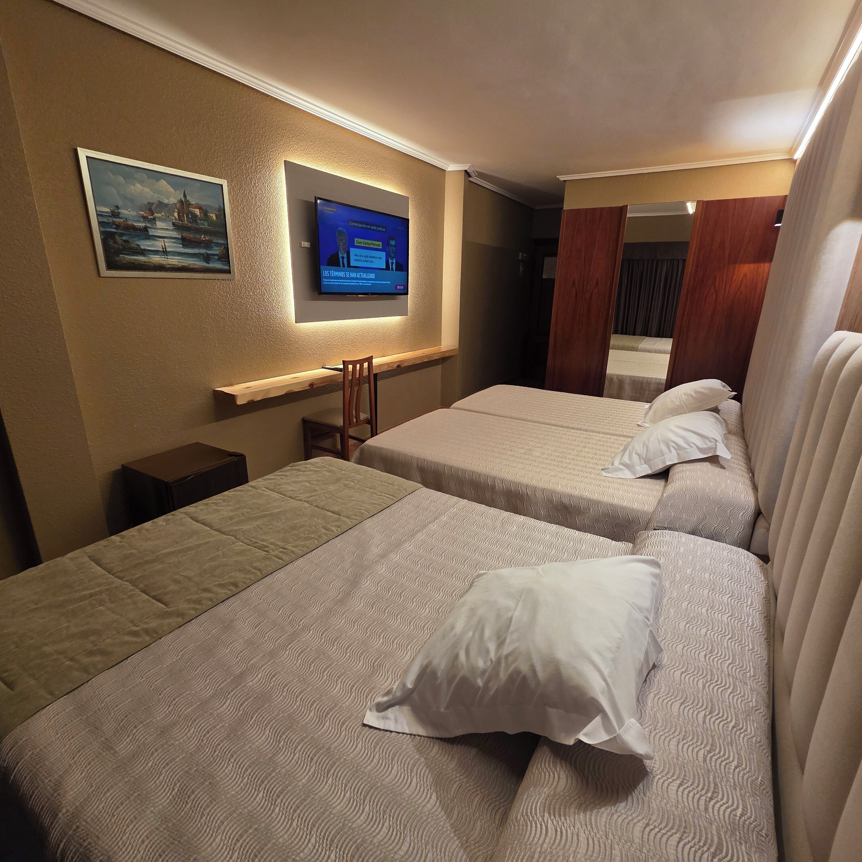 A hotel room with two beds, a TV mounted on the wall, and a painting above the TV.