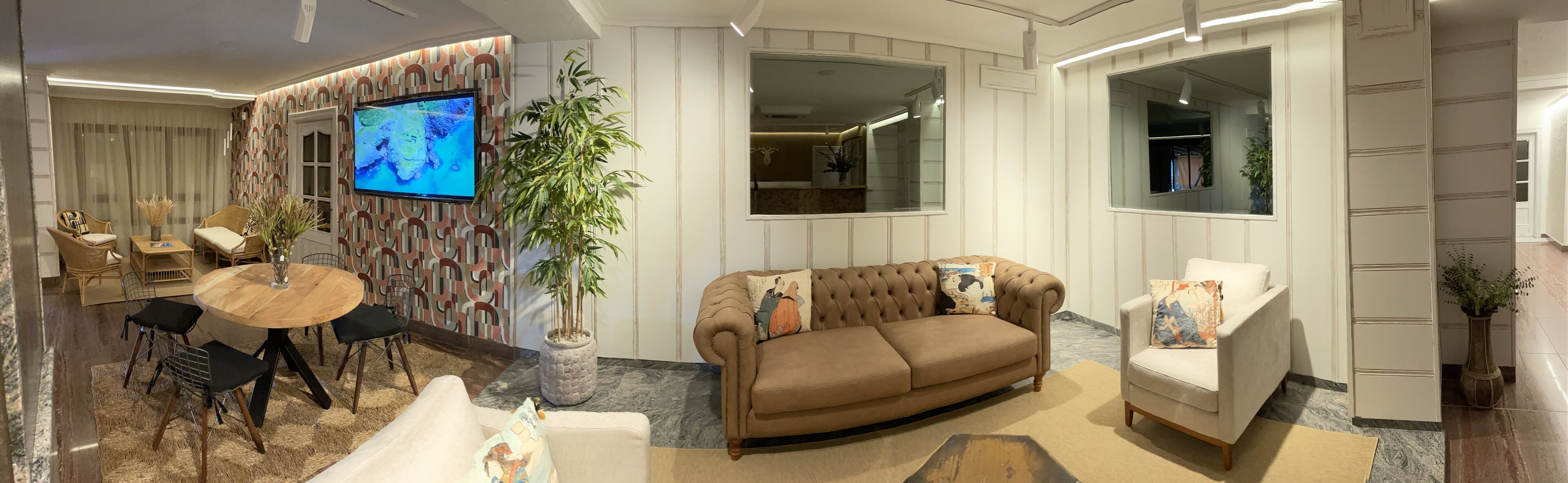 A modern living room with a brown sofa, a white armchair, a wooden coffee table, and a TV mounted on the wall.