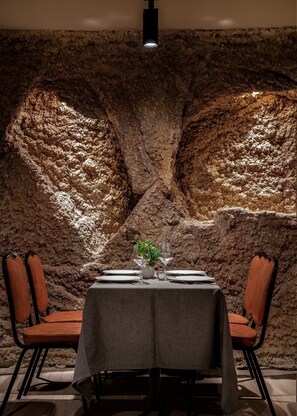 A table set for two with a rustic stone wall backdrop, a small plant centerpiece, and modern chairs. - Hotel Gala (Noja)