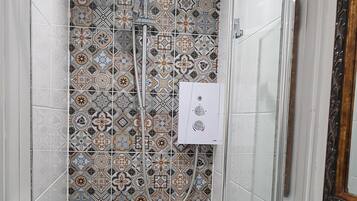 A shower with a glass door and a tiled wall with a geometric pattern.
