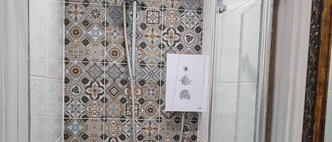 A shower with a glass door and a tiled wall with a geometric pattern.