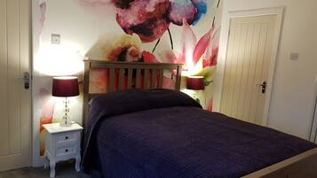 A bedroom with a bed, two bedside lamps, a nightstand, and a floral wall mural.