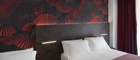 Una habitación de hotel con una cama grande, dos mesitas de noche y una pared con un estampado de abanicos rojo y negro.