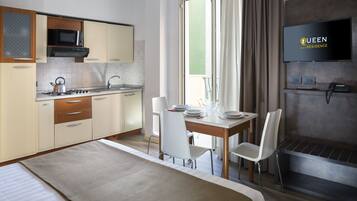 Una habitación de hotel moderna con kitchenette, comedor con mesa y sillas, cama, televisor y teléfono.