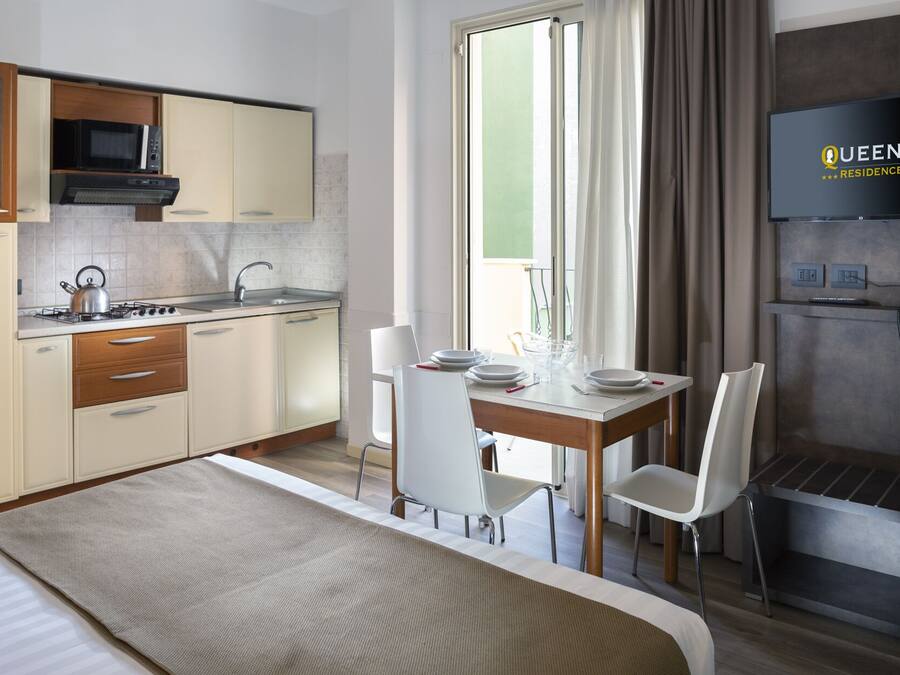 Una habitación de hotel moderna con kitchenette, comedor con mesa y sillas, cama, televisor y teléfono.