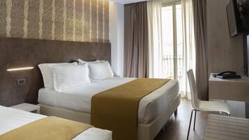 Una habitación de hotel con una cama grande, una cama más pequeña, un escritorio con una silla y un televisor.
