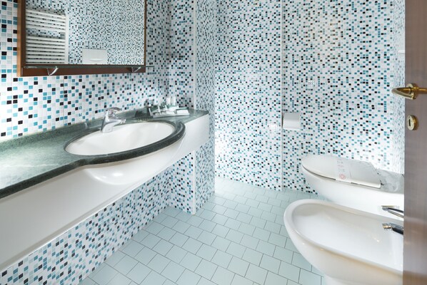 Un baño con un lavabo blanco, un espejo y un inodoro. Las paredes están cubiertas de un mosaico azul y blanco.