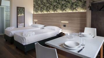 A hotel room with two beds, a dining area with a table set for two, and a wall with a fern leaf pattern.