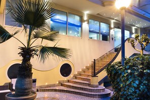 Una escalera con barandilla, una palmera y un muro con ventanales redondos.