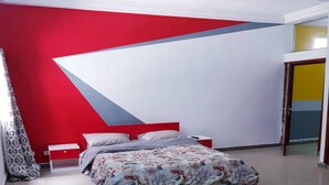 Um quarto com uma cama, uma mesa de cabeceira, uma parede vermelha e uma porta.