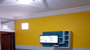 Um quarto com parede amarela, teto com luz embutida e televisão fixada na parede.