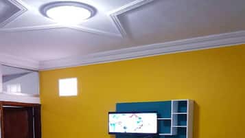 Une pièce avec un mur jaune, un plafond doté d’un éclairage encastré et un téléviseur fixé au mur.
